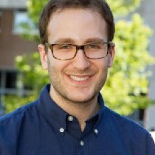 Portrait of Daniel Bessner in a blue shirt and glasses