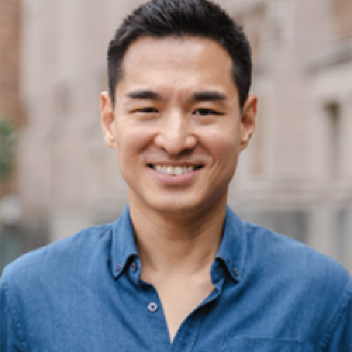 Jang Wook Huh stands outside in front of a building wearing a blue shirt.