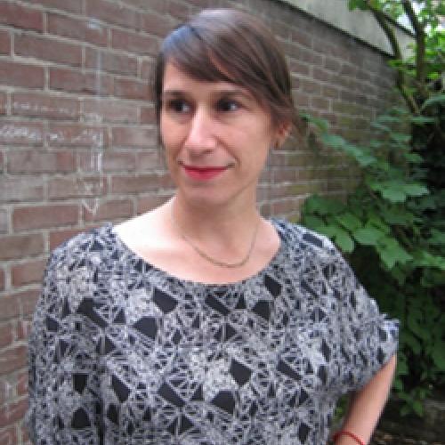 Jenna Grant stands outside in front of a brick wall wearing a patterned shirt. 