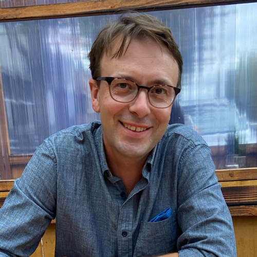 A close-up image of Jesse Oak Taylor wearing a blue shirt and glasses.