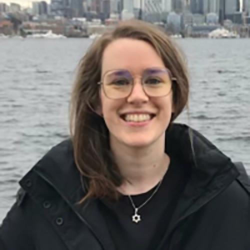 Kaelie Giffel stands in front of water wearing a dark coat and glasses.