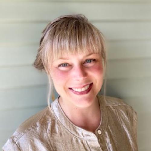 Kate Krieg stands in front of a shiplapped wall while wearing a light-colored shirt.