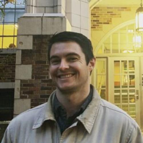 Kyle Kubler stands in front of a brick wall wearing a light jacket.