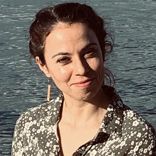 A portrait of Leah Rubinsky standing in front of a body of water.