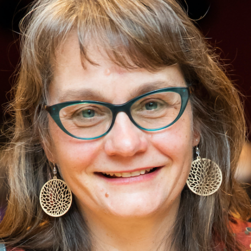 Portrait of Lynn Thomas wearing glasses and yellow dangle earrings.