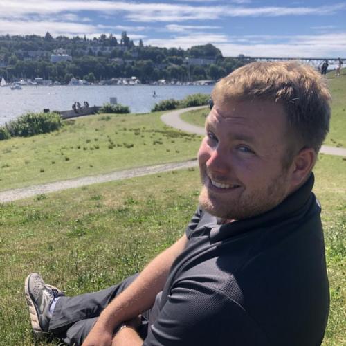 Matthew Childs sits outside on a hill overlooking a body of water.