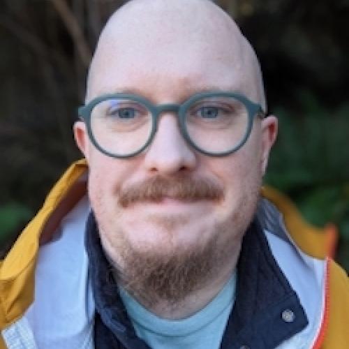 Matthew Poland looks at the camera while wearing green glasses.