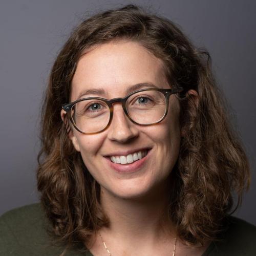 Headshot of Melanie Walsh standing in front of a grey wall wearing glasses.