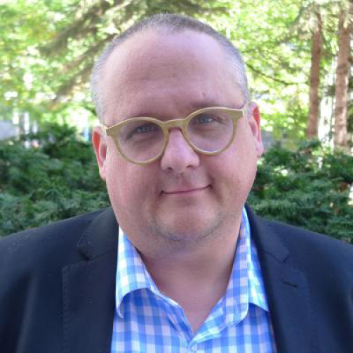 Portrait of Michael Blake wearing a suit and sitting outside.