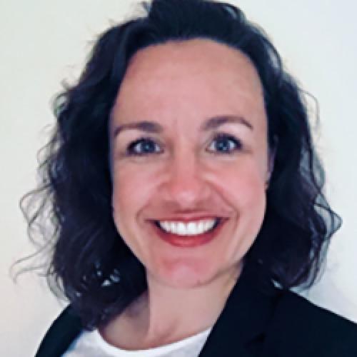 Kristina Pilz wears a white shirt and black jacket while standing in front of a white wall.