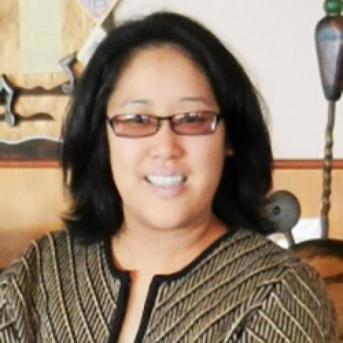 Portrait of Regina Yung Lee wearing glasses and sitting in front of a light wall.