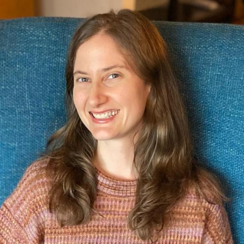 Adair Rounthwaite sits on a blue chair wearing a pink sweater. 