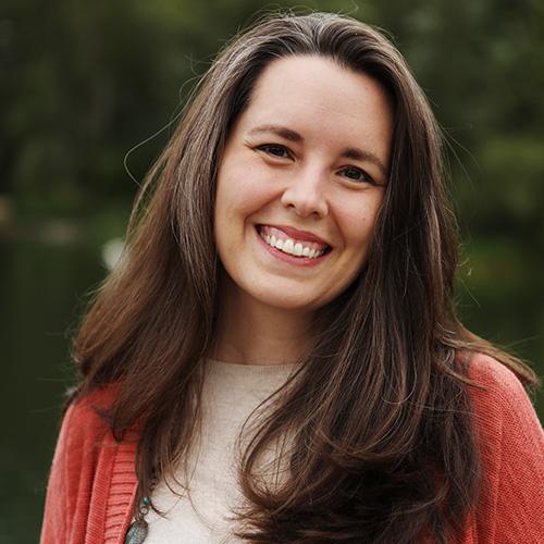 Sarah Moore stands outside while wearing a read cardigan and white shirt.