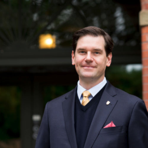 Guillaume Tourniaire stands in front of a blurred out doorway wearing a suit and tie.