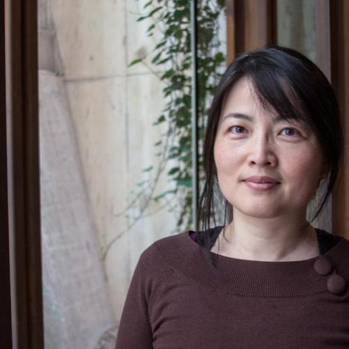 Ping Wang stands in front of a window wearing a brown shirt.