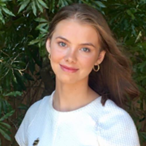 Anna Bates stands in front of plants and wears a white shirt.