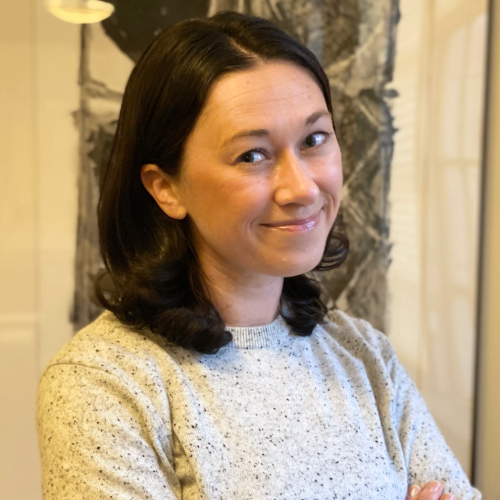 Rachel Arteaga smiling at the camera in a grey sweater, arms folded.