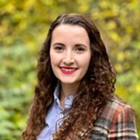 Laura Gehrke stands outside wearing a blue collared shirt and plaid jacket.