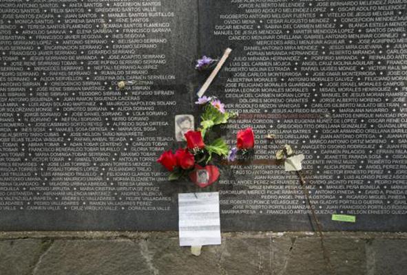 A bouquet of flowers sits at the base of a dark wall with names etched in white.