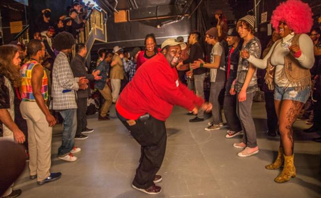 A person in a red shirt dances while surrounded by other people.