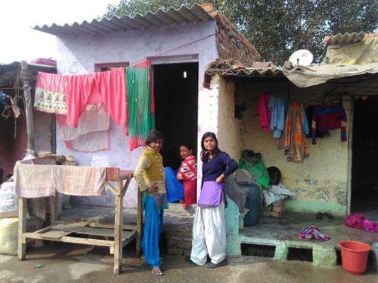 Three women sit or stand near a building's doorway with colorful laundry hanging around them.