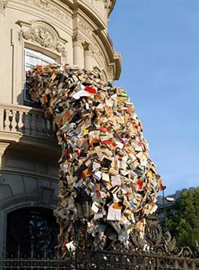 A sculptural installation by Alicia Martin at Casa de America, Madrid, of a wave made of thousands of books falling from a second-story window to the ground.