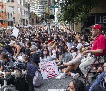 Protesters participating n the Seattle Youth Protest sit in the intersection outside the Seattle Police Department. One protester holds a sign reading, "Justice 4 Breonna Taylor"