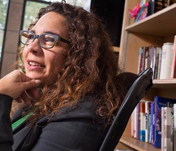 Ralina Joseph sits in front of a bookcase wearing glasses and a dark jacket.