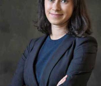 Rachel Arteaga looks into the camera wearing a blue shirt and dark blazer against a gray background.