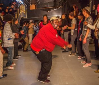 A person in a red shirt dances while surrounded by other people