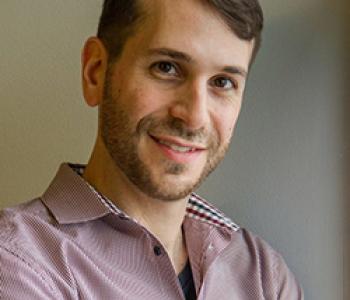 Abraham Avnisan stands in front of a white wall wearing a patterned shirt. 