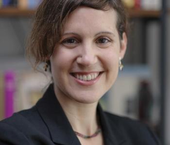 Mika Ahuvia in suit jacket smiling with bookcase in background 