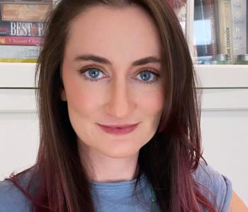 Close-up portrait of a white woman with pink and brown hair and blue eyes wearing a blue shirt