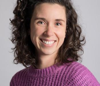 Audrey Desjardins stands in front of a white wall while wearing a lavender knit sweater.