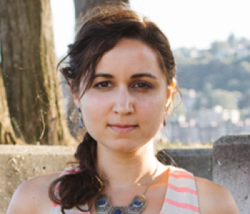 Anjuli Brekke stands in front of a tree and a landscape of houses while wearing a striped sleeveless top and a necklace.