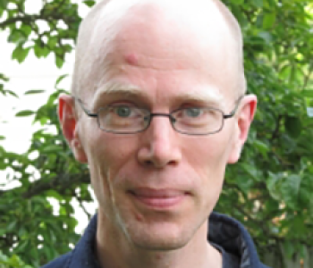 Portrait of Charles LaPorte wearing glasses and standing in front of a tree.