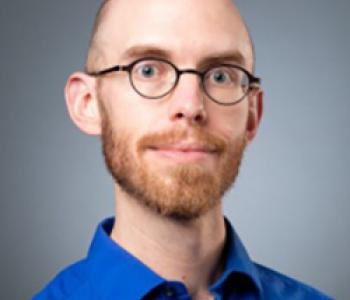 Portrait of Colin Marshall wearing a blue shirt and glasses.