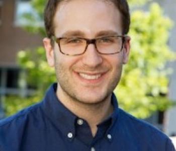 Portrait of Daniel Bessner in a blue shirt and glasses