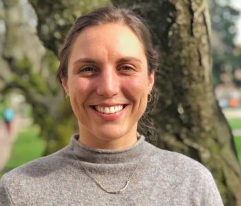 A portrait of Erika Versalovic standing in front of a tree wearing a grey sweater.