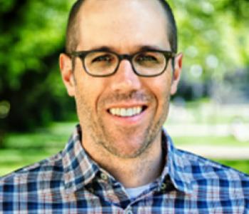 Portrait of Ian Schnee wearing glasses and standing outside.