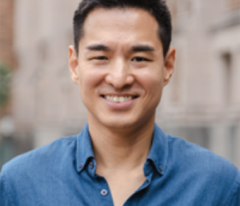 Jang Wook Huh stands outside in front of a building wearing a blue shirt.