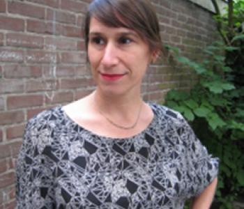 Jenna Grant stands outside in front of a brick wall wearing a patterned shirt. 