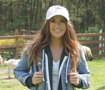 Jessica Holmes stands outside wearing white cap and denim jacket.
