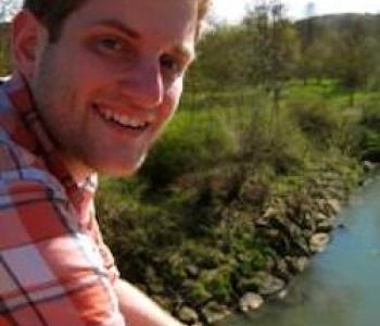 Justin Mohler looks at the camera while sitting in front of a river.