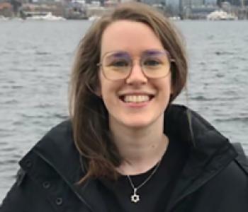 Kaelie Giffel stands in front of water wearing a dark coat and glasses.