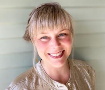 Kate Krieg stands in front of a shiplapped wall while wearing a light-colored shirt.