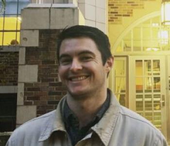 Kyle Kubler stands in front of a brick wall wearing a light jacket.