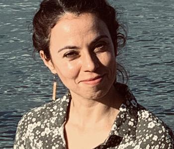 A portrait of Leah Rubinsky standing in front of a body of water.