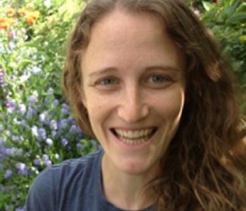 Lily Shapiro stands in front of a bush wearing a blue shirt.