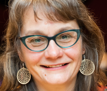 Portrait of Lynn Thomas wearing glasses and yellow dangle earrings.